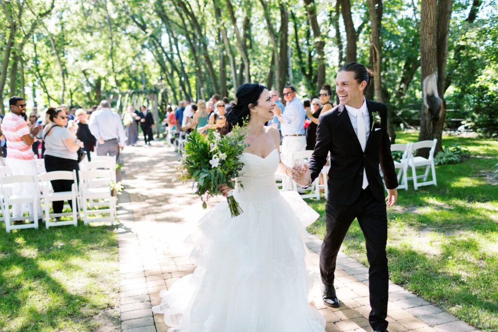 Bride and Groom walking out from their ceremony in joyful moment looking at each other as husband and wife at Carlos Creek Winery in Alexandria, MN, captured by Minnesota wedding photographer Toly Dzyuba. 