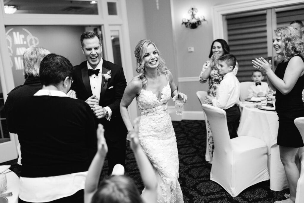 Guests cheering as bride and groom enter their reception with smiles and energy.