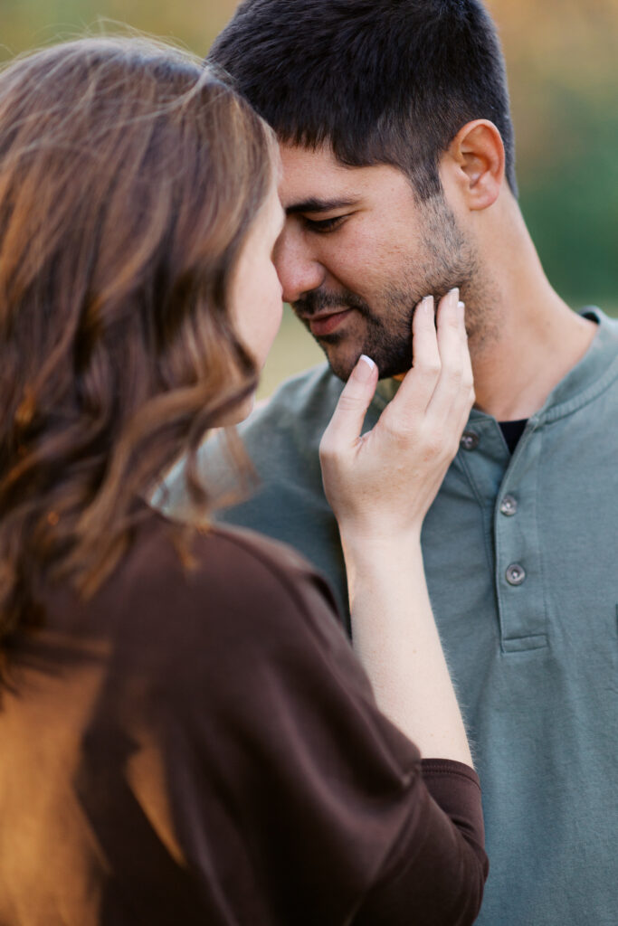 She gently touches his face as they touch with their foreheads at Romantic Elm Creek Park Engagement Session in Maple Grove, Minnesota.