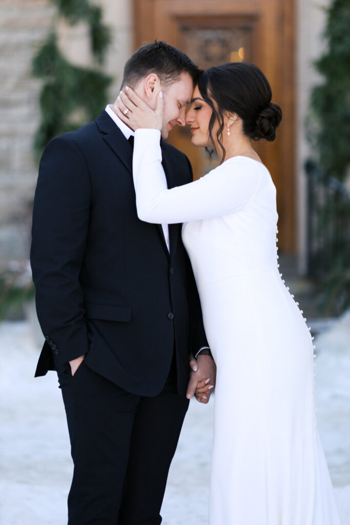 Romantic bride and groom portraits in snow with bride and groom eyes closed and touching heads at St. Paul College Club by Minneapolis wedding photographer.