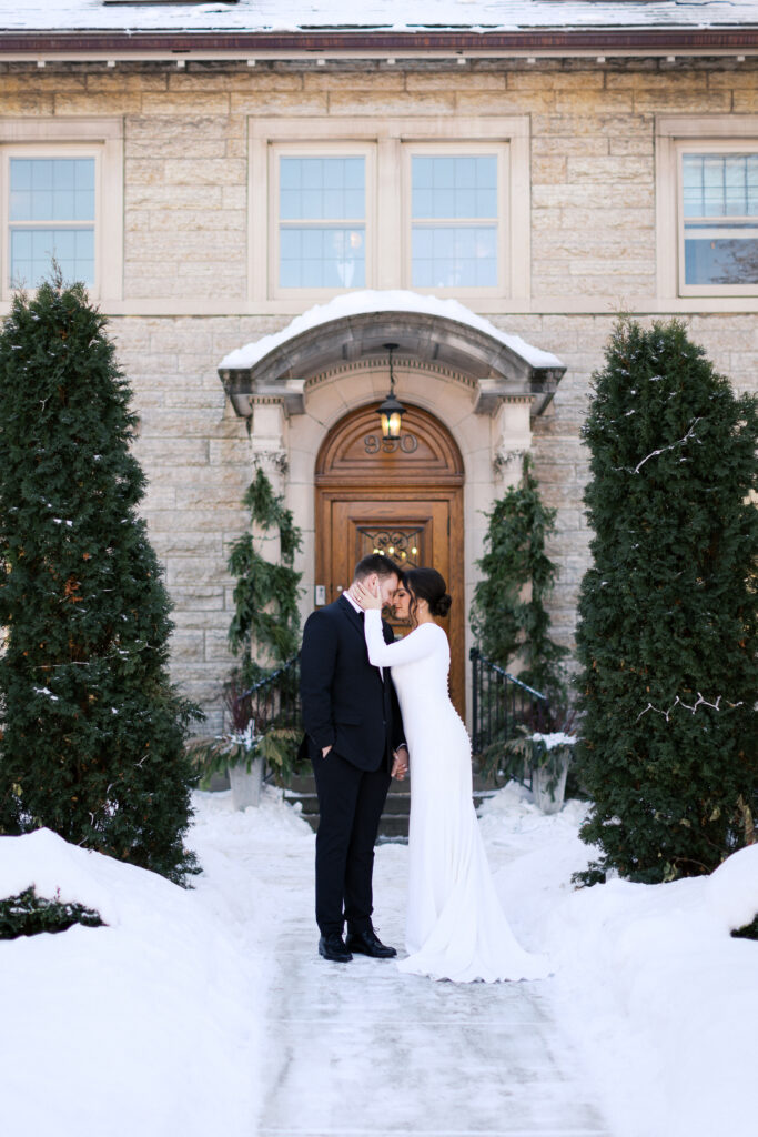 Snowy wedding portraits outside St. Paul College Club with bride and groom standing next to each other with heads together, captured by Minnesota wedding photographer.