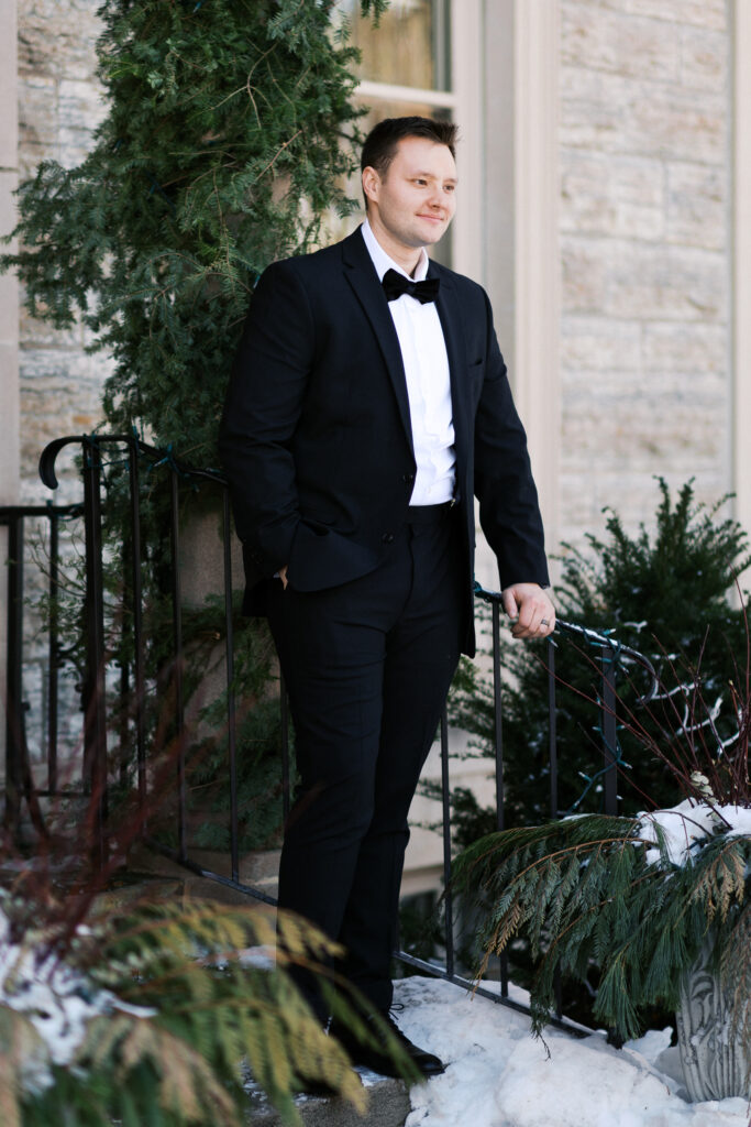 Portrait of the groom in his black suit looking away with his hand in a pocket at St. Paul College Club captured by Minnesota wedding photographer.