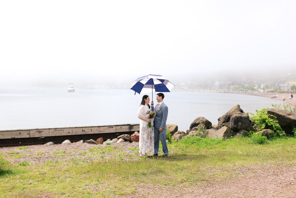 Minnesota wedding photographer captures intimate moment of the newlyweds standing under the umbrella by the The Mayhew Inn.