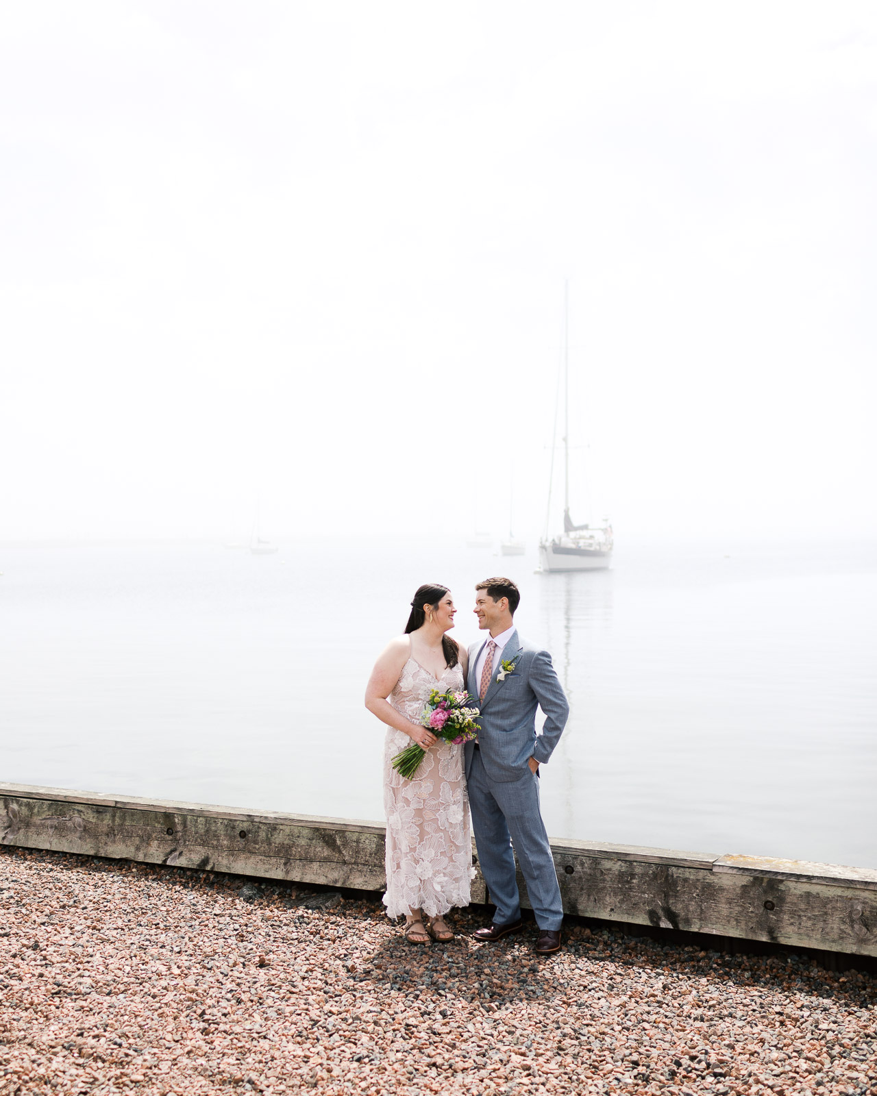 Newly weds stand tall looking at each other at The Mayhew Inn wedding with Lake Superior as their backdrop, captured by Minneapolis wedding photographer.